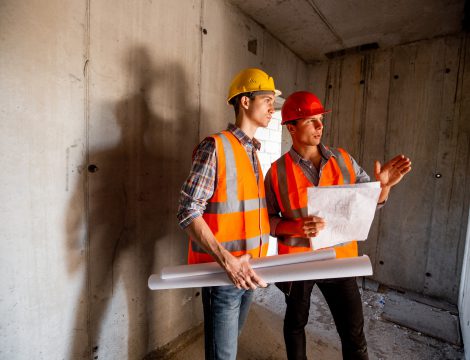 Construction manager and engineer dressed in orange work vests and helmets work with construction