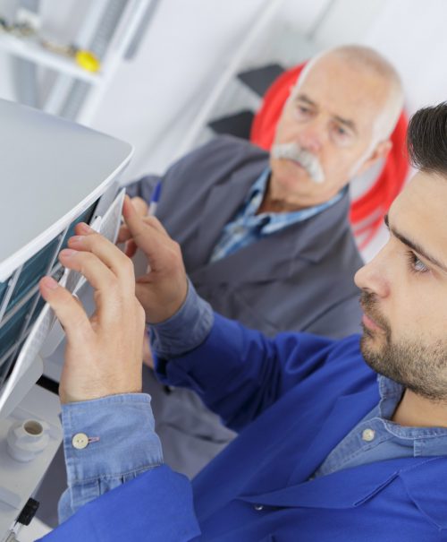 male technician is repairing a printer assited by senior